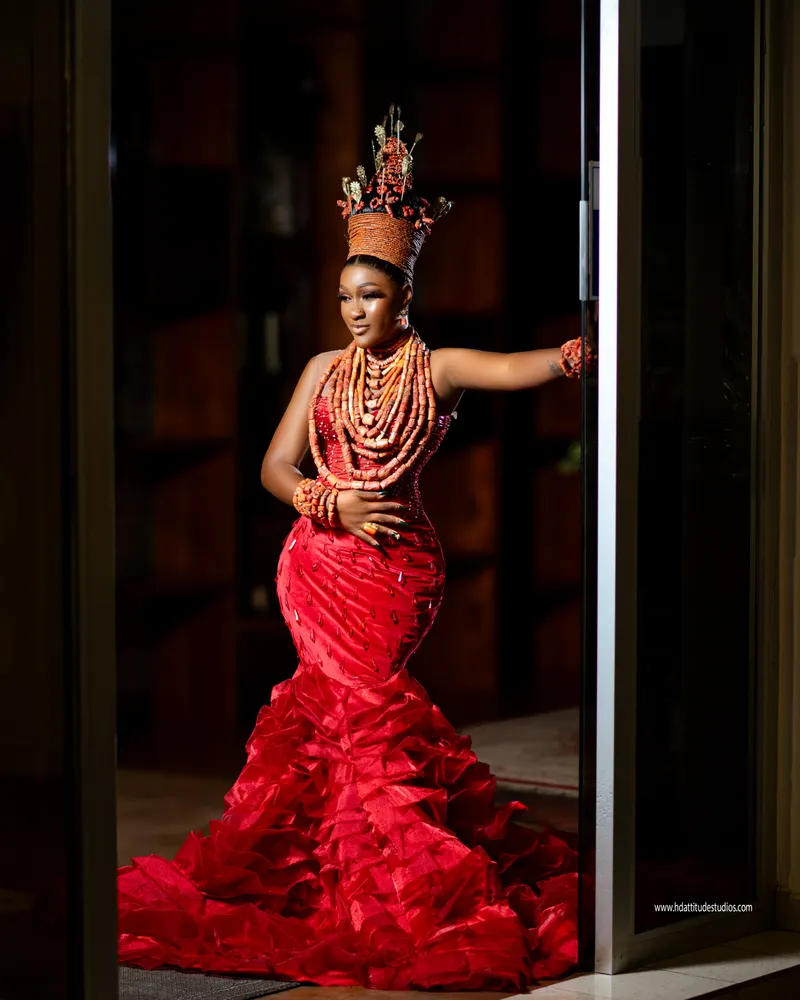 Same coral-crowned bride standing in doorway, hand on door frame, backlit